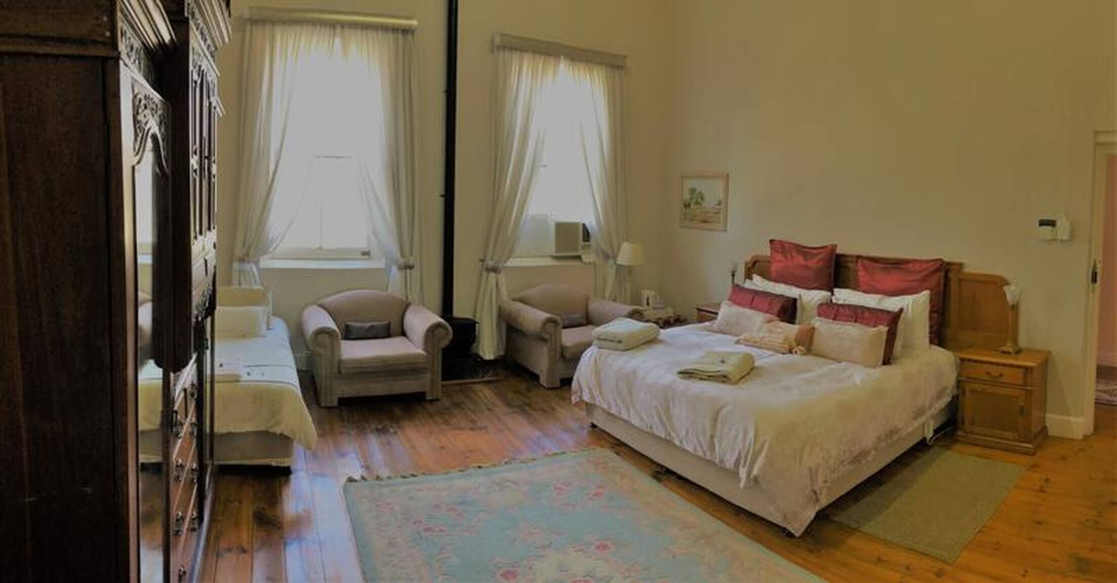 Une chambre à coucher avec un lit, deux chaises, une table de chevet, une lampe et une fenêtre avec des rideaux.