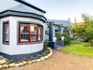 A house with a curved corner, a gravel driveway, and a garden with plants and a tree.