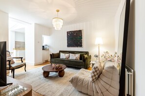 A living room with a sofa, a coffee table, and a TV. There is a kitchen in the background. - Stylish Bloomsbury Two-Bed Retreat (London)