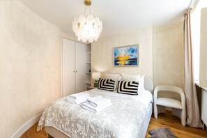 Een hotelkamer met een bed, een stoel, een kledingkast, een schilderij en een kroonluchter.