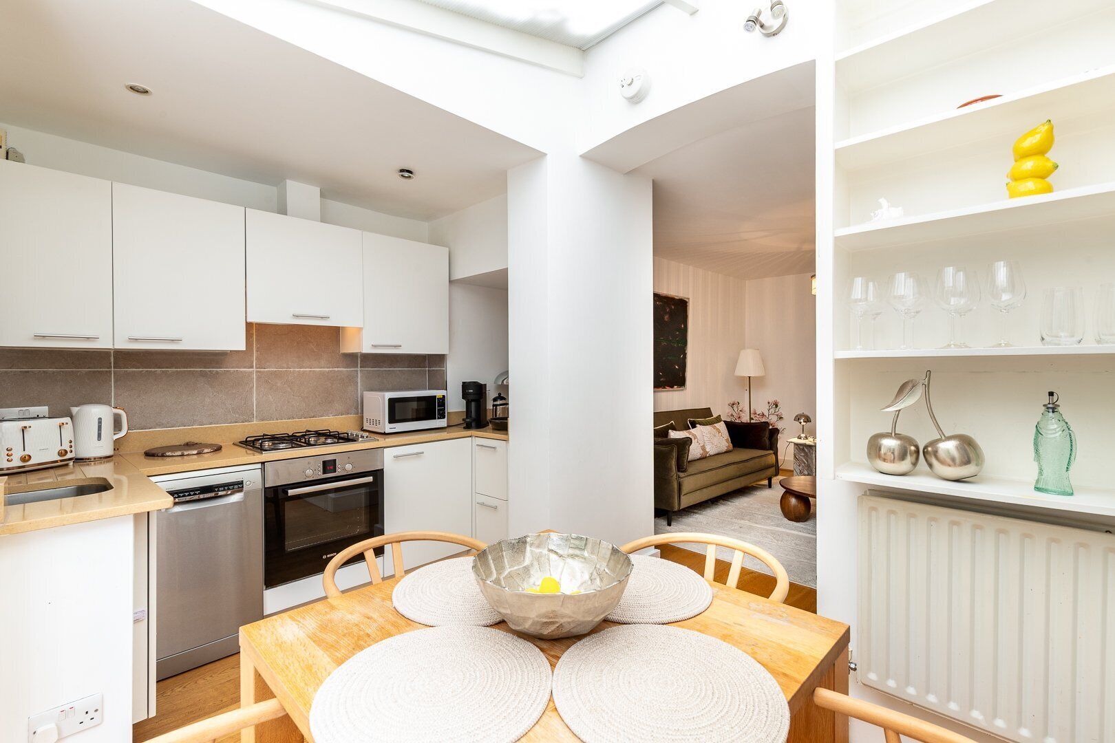 A modern kitchen with white cabinets, a dining table with placemats, and a living area with a sofa and a coffee table.