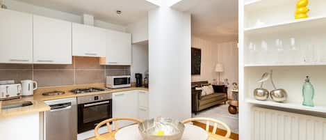 A modern kitchen with white cabinets, a dining table with placemats, and a living area with a sofa and a coffee table.