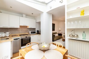 A modern kitchen with white cabinets, a dining table with placemats, and a living area with a sofa and a coffee table. - Stylish Bloomsbury Two-Bed Retreat (London)