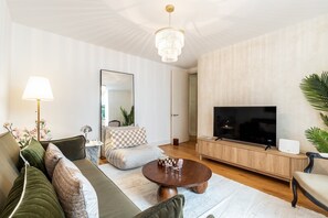 Een moderne woonkamer met een bank, fauteuil, salontafel, televisie en een kroonluchter.