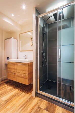 A modern bathroom with a glass-enclosed shower, a wooden vanity with drawers, and a white sink. - Fully equipped new 2BR 2BA one BR/BA individual entrance in Central Paris (Paris)