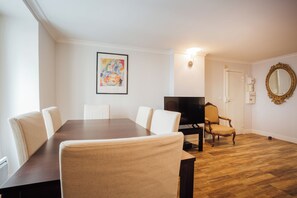 A dining area with a dark wooden table and beige upholstered chairs, a television, and a decorative mirror on the wall. - Fully equipped new 2BR 2BA one BR/BA individual entrance in Central Paris (Paris)
