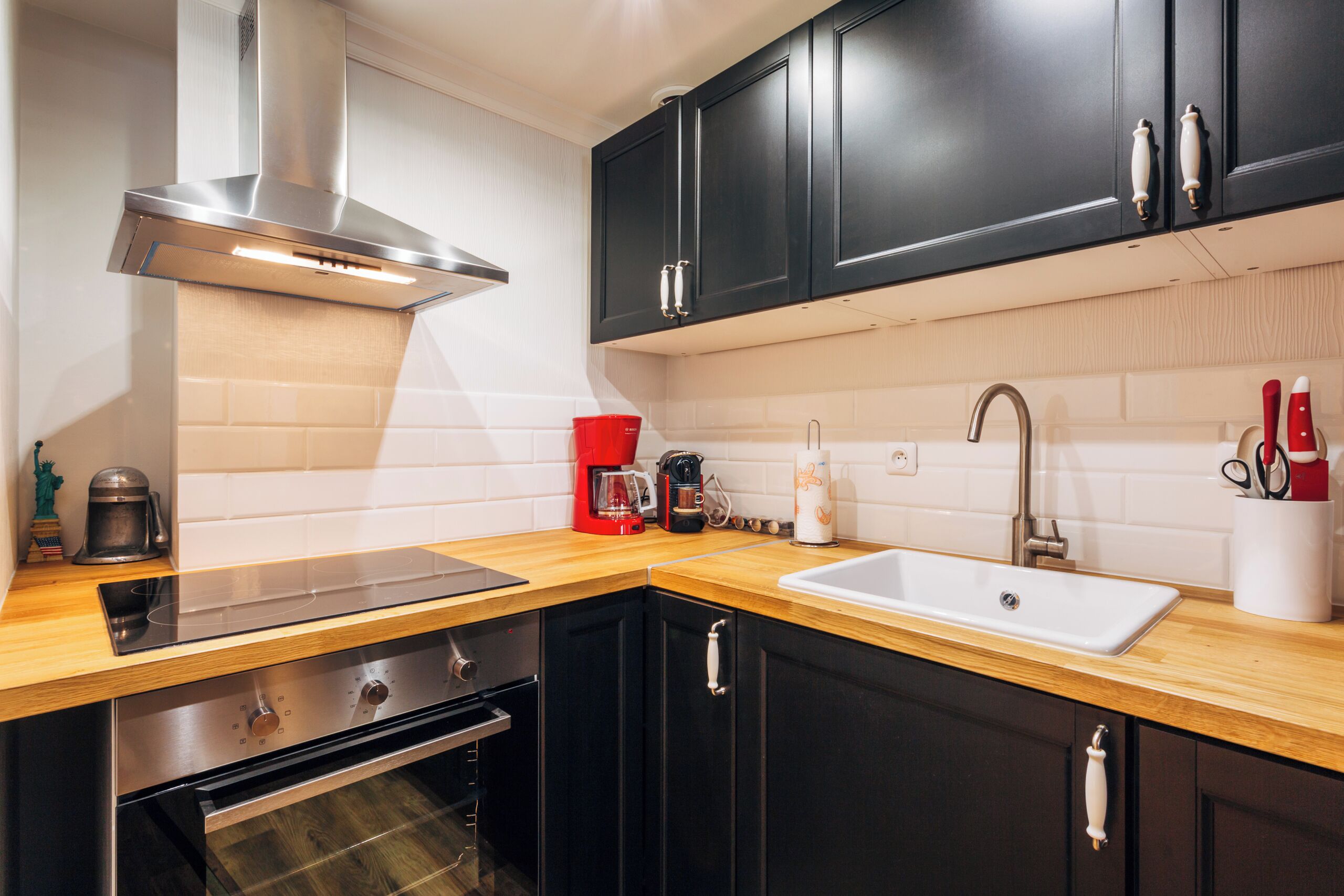 Une cuisine moderne avec des meubles de couleur noire, une hotte de cuisinière en acier inoxydable, un plan de travail en bois, un évier et une machine à café.