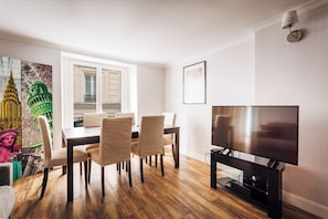 A modern living room with a dining area, a flat-screen TV, and a large window.