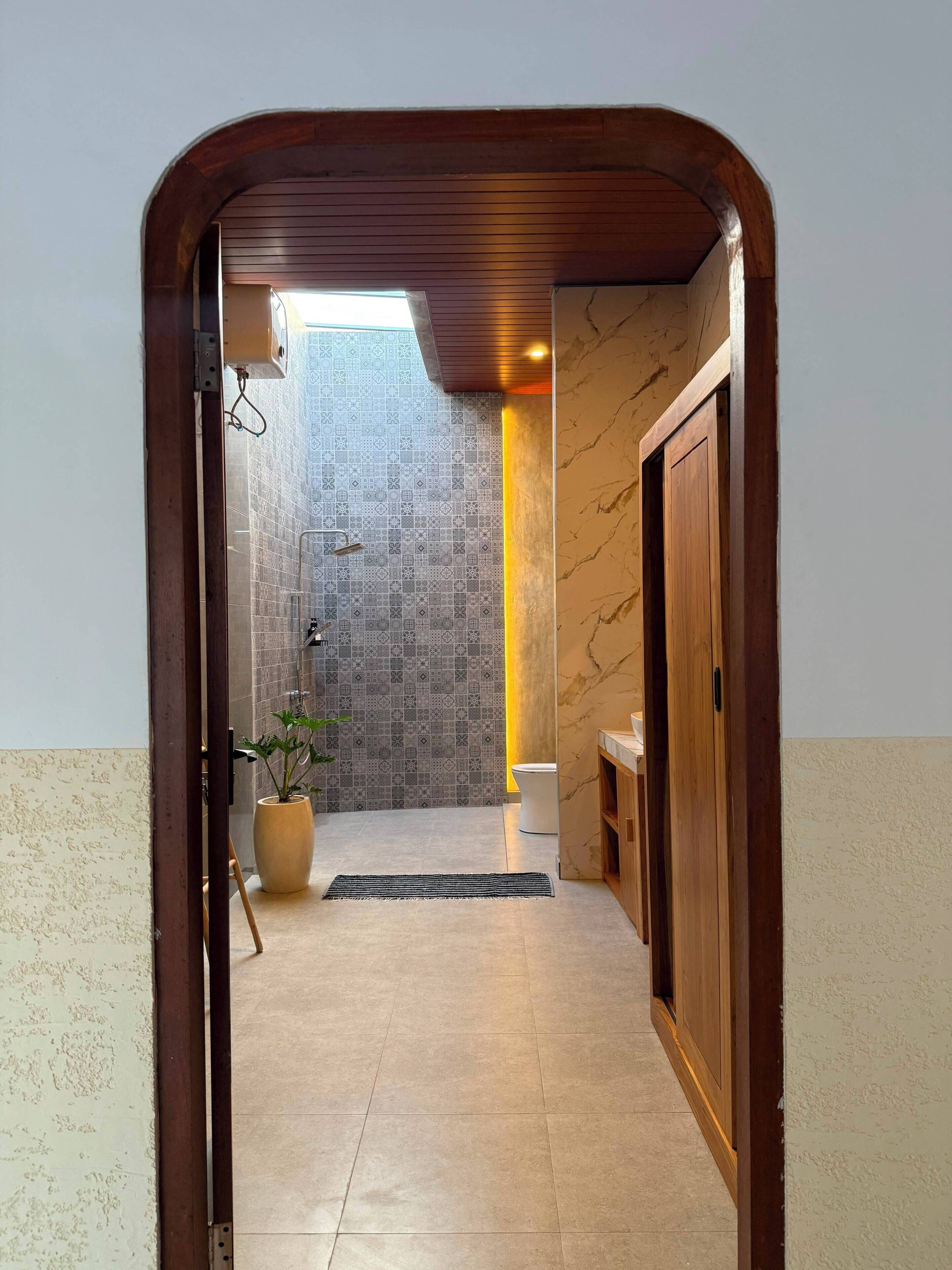 Un pasillo con pared de azulejos, una planta en maceta, una puerta de madera y piso de baldosas.