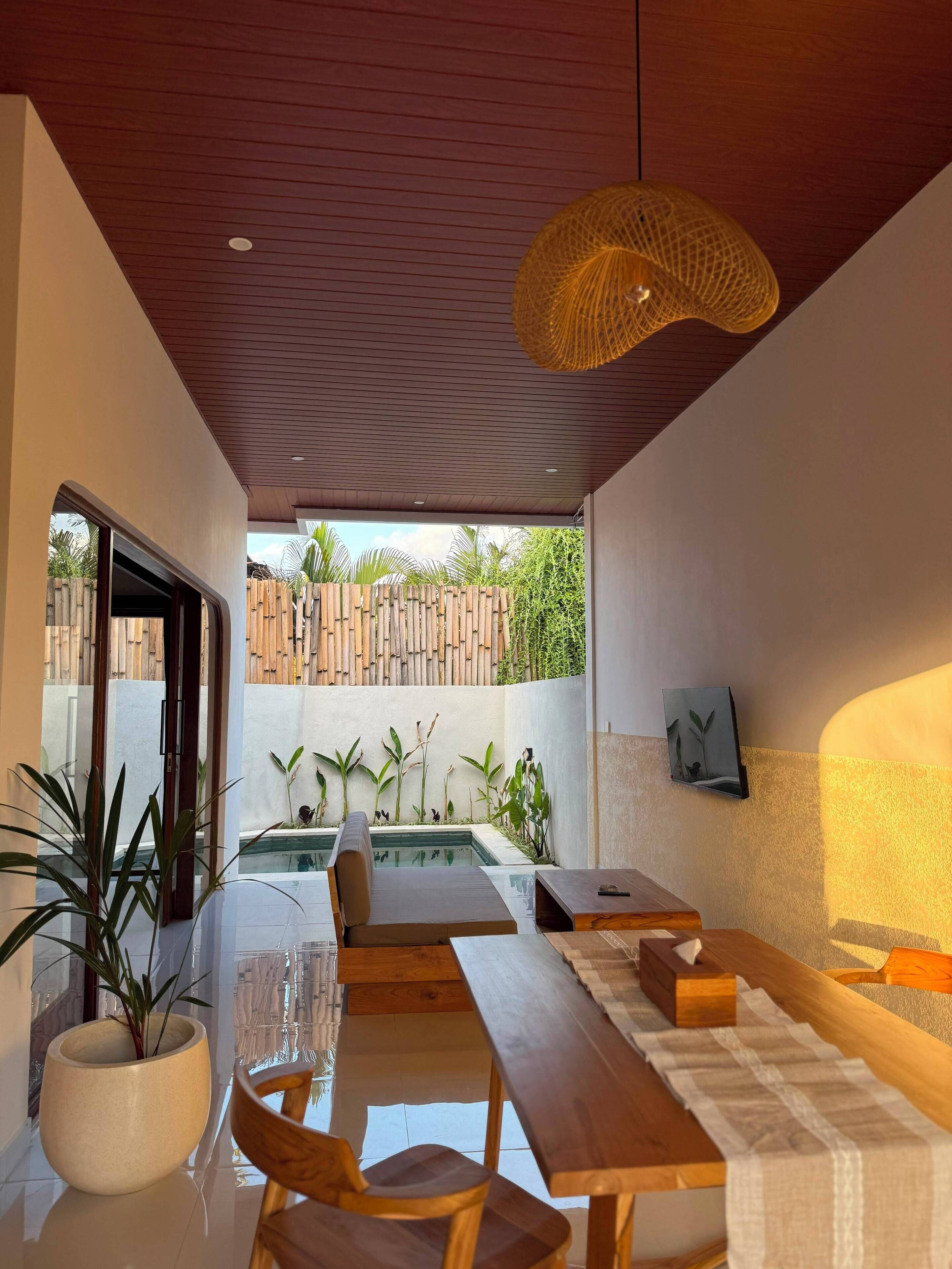 Un comedor interior con vistas a la piscina, muebles de madera y una lámpara colgante.