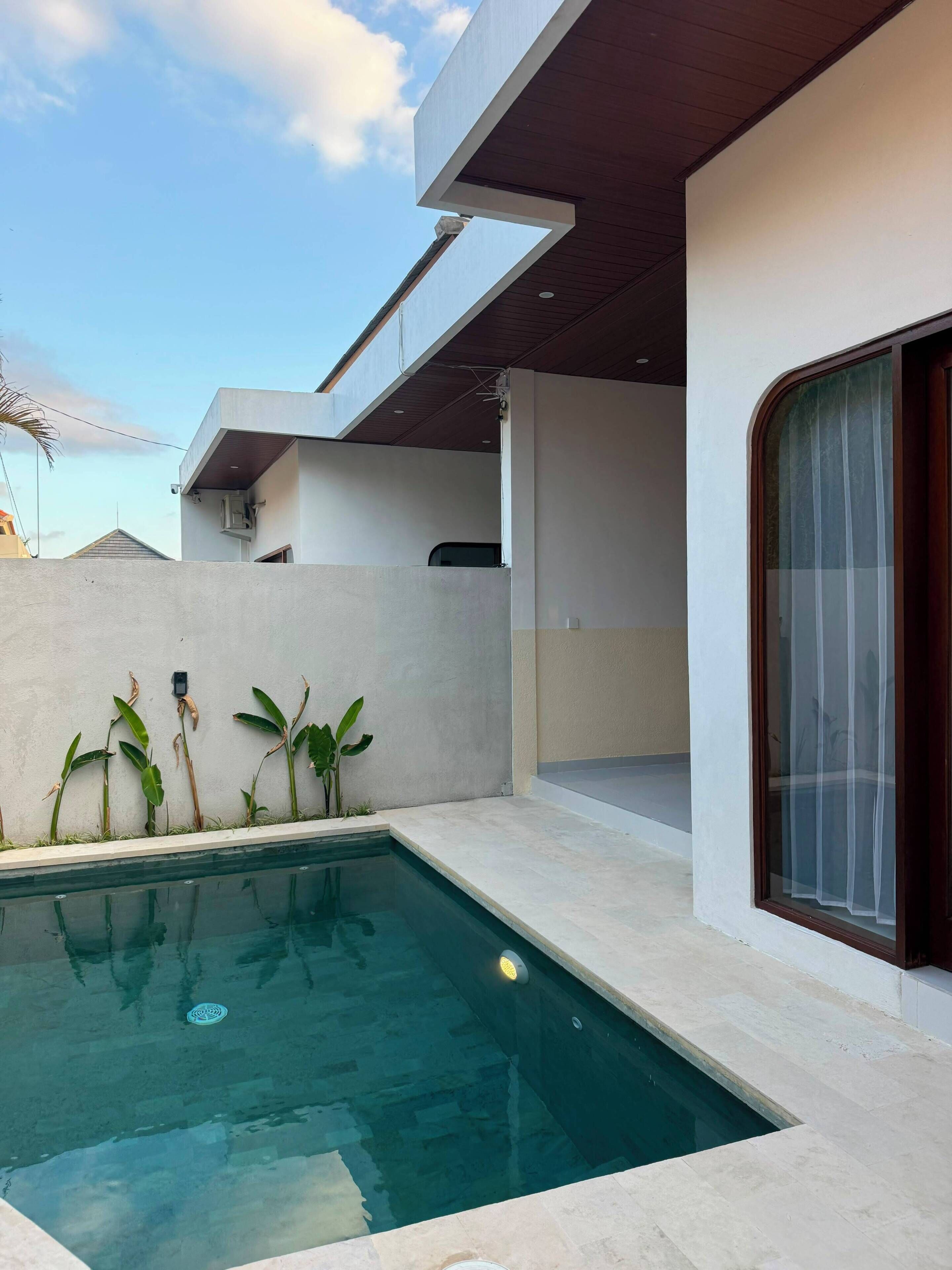Un área de piscina moderna al aire libre con una piscina cristalina, una zona de estar cubierta y vistas al cielo.