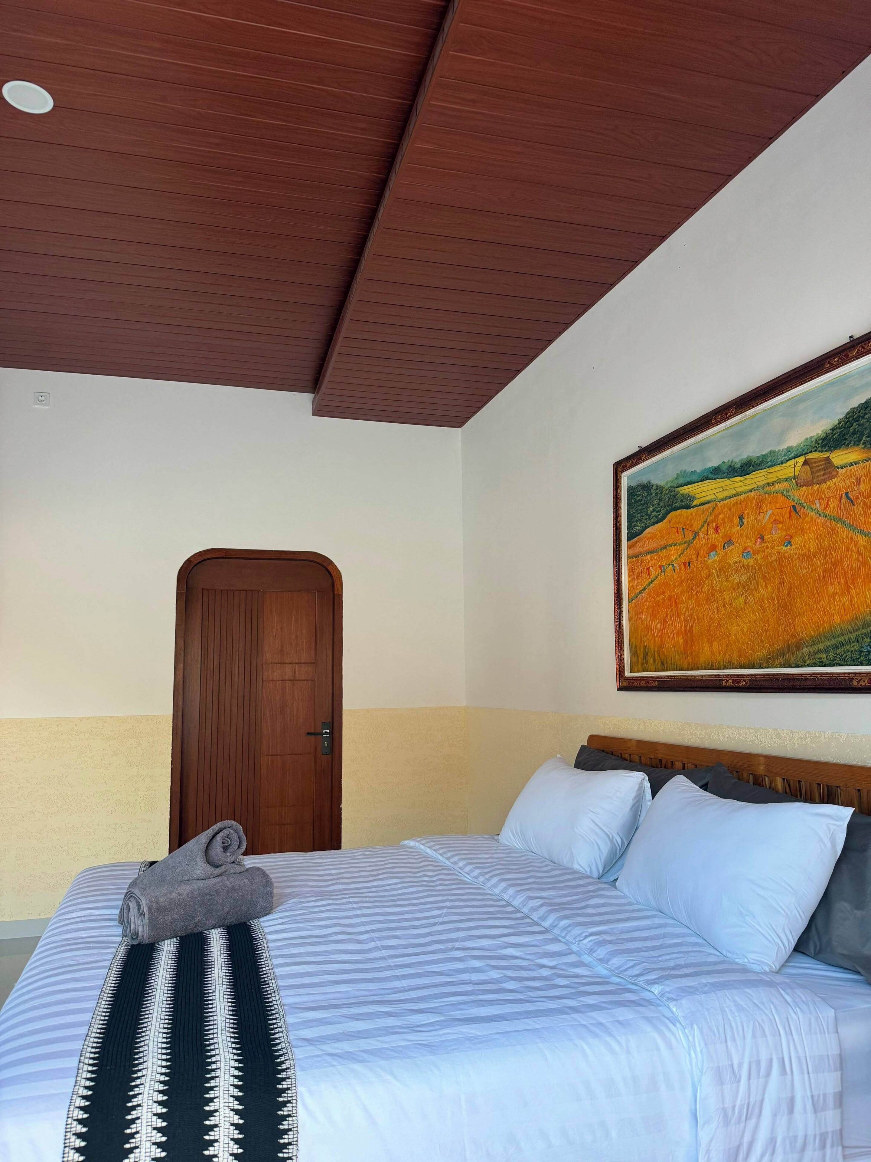 Habitación de hotel con una cama, un cuadro, una puerta de madera y un techo con diseño decorativo.
