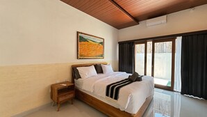 A hotel room with a large bed, a nightstand, a painting on the wall, and a view through a window. - BUBU Villa Ubud  (Ubud)