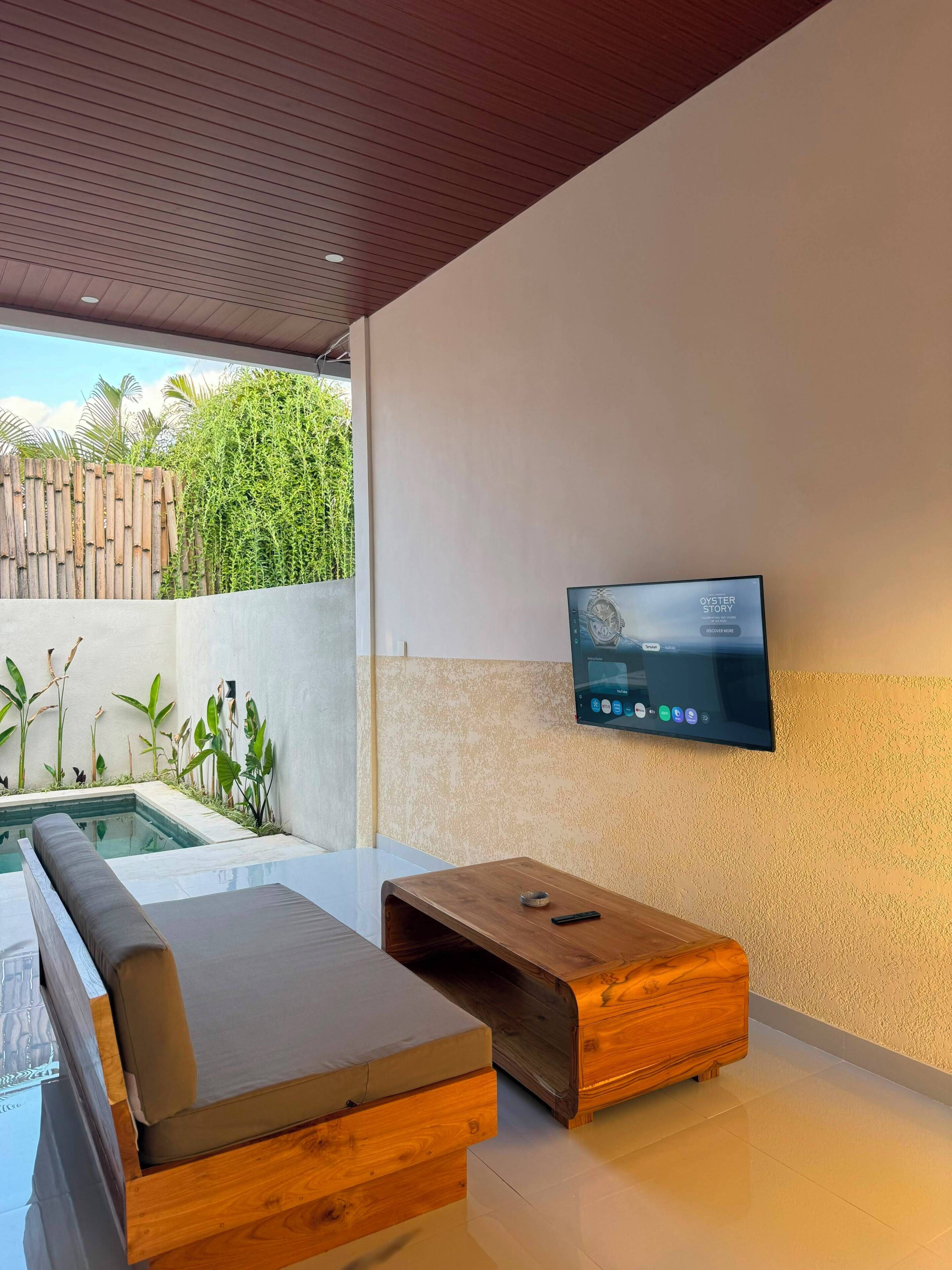 Un área de estar moderna al aire libre con piscina, un televisor de pantalla plana en la pared y un banco de madera.