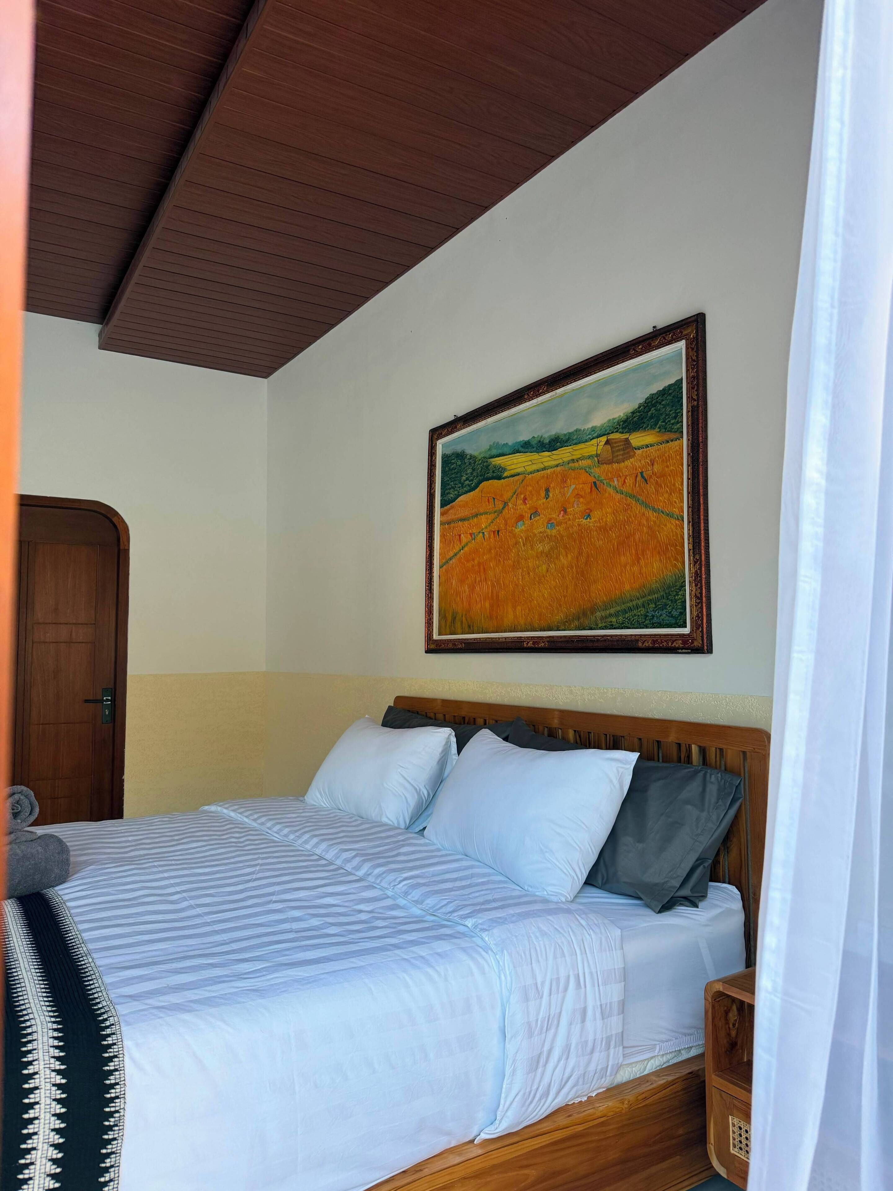 Una habitación con una cama, cabecera de madera, un cuadro en la pared y una puerta.