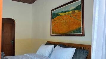 Una habitación con una cama, cabecera de madera, un cuadro en la pared y una puerta.