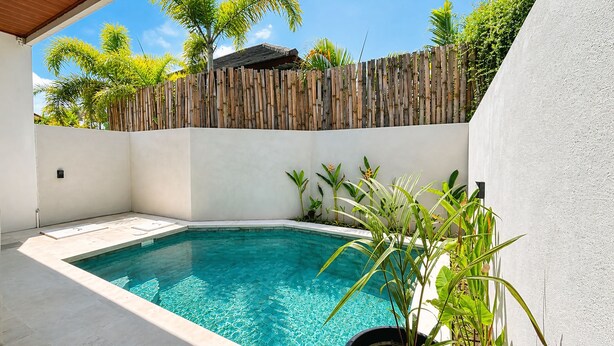 A swimming pool with a bamboo fence, surrounded by tropical plants and a white wall. - BUBU Villa Ubud  (Ubud)