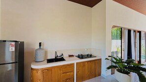 A modern kitchen with wooden cabinets, a stainless steel refrigerator, a gas stove, and a large vase of green plants. - BUBU Villa Ubud  (Ubud)