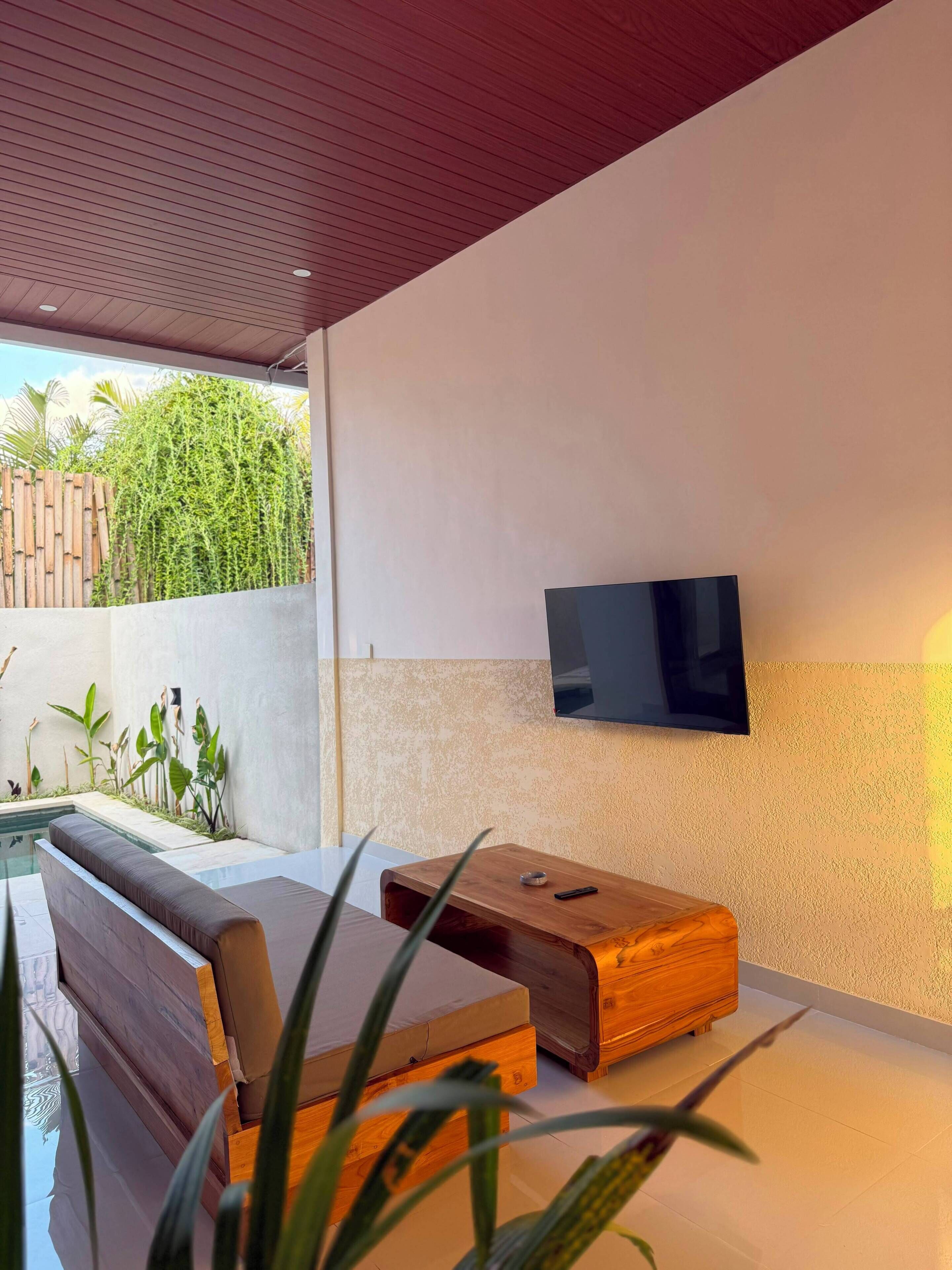 Een moderne buitenruimte met zitgelegenheid, een flatscreen televisie aan de muur, een comfortabele bank en een houten tafel.