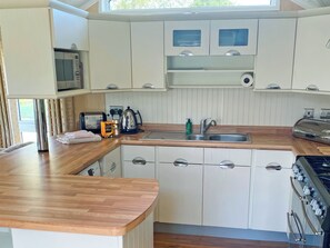 A compact kitchen with white cabinets, a wooden countertop, a built-in microwave, a kettle, and a stove. - 2 bedroom accommodation in Newquay (Newquay)