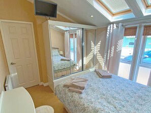 A bedroom with a bed, a TV mounted on the wall, a window with curtains, and a view of the outside. - 2 bedroom accommodation in Newquay (Newquay)