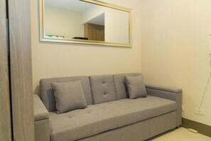 A grey sofa with three cushions against a wall, a mirror above it, and a power outlet to the right. - Elegant Stay in Prime Location for Traveler Near BGC, Makati, Ortigas & MRT (Mandaluyong City)