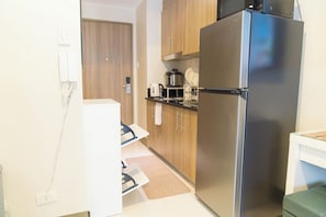 A compact kitchen with a stainless steel refrigerator, wooden cabinets, and a small countertop with a kettle and a coffee maker. - Elegant Stay in Prime Location for Traveler Near BGC, Makati, Ortigas & MRT (Mandaluyong City)