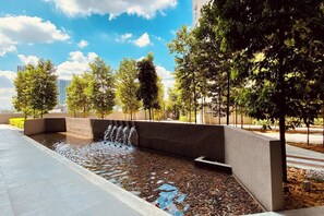 Un élément décoratif aquatique composé de plusieurs jets d’eau, entouré d’arbres et bordé d’une allée pavée.