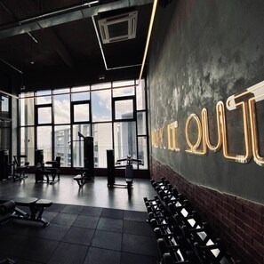 Une salle de sport équipée de matériel d’exercice, dotée de grandes fenêtres et d’un mur sur lequel est affiché un texte lumineux.