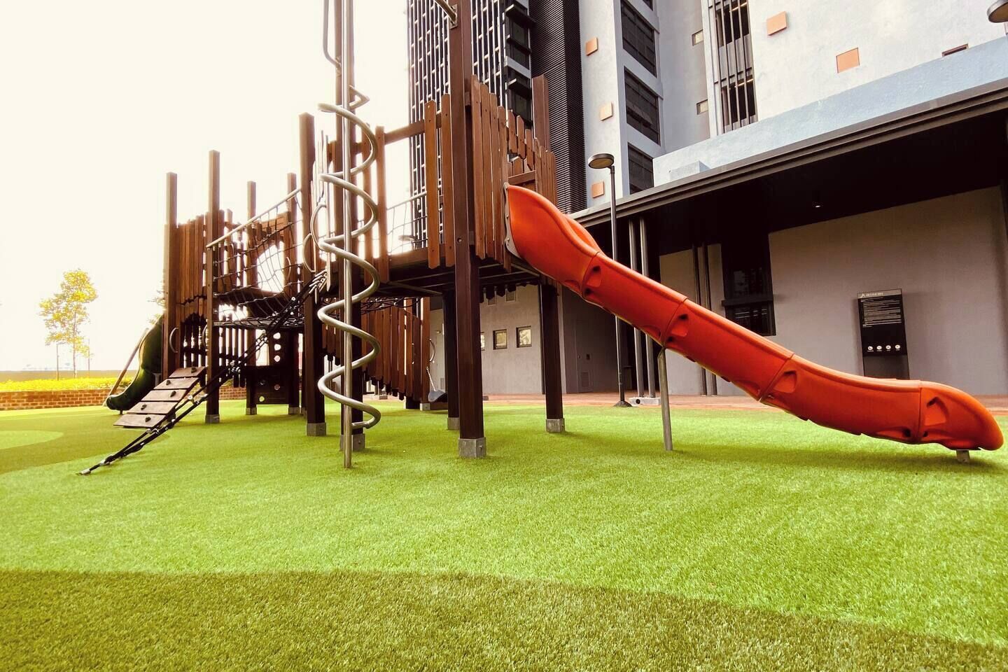 A playground with a slide and climbing structures, set against a building facade.