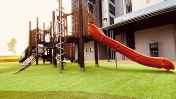A playground with a slide and climbing structures, set against a building facade.