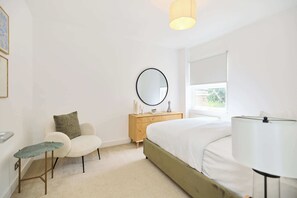 Ein Schlafzimmer mit Bett, Nachttisch, Lampe, Stuhl und einem Fenster mit Blick.