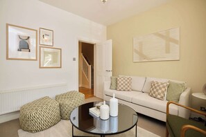 Ein Wohnzimmer mit einer Couch, Poufs, einem Couchtisch und gerahmten Kunstwerken an der Wand.