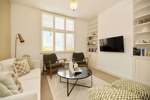 Ein Wohnzimmer mit einer Couch, zwei Sesseln, einem Couchtisch, einem Fernseher und einem Bücherregal.