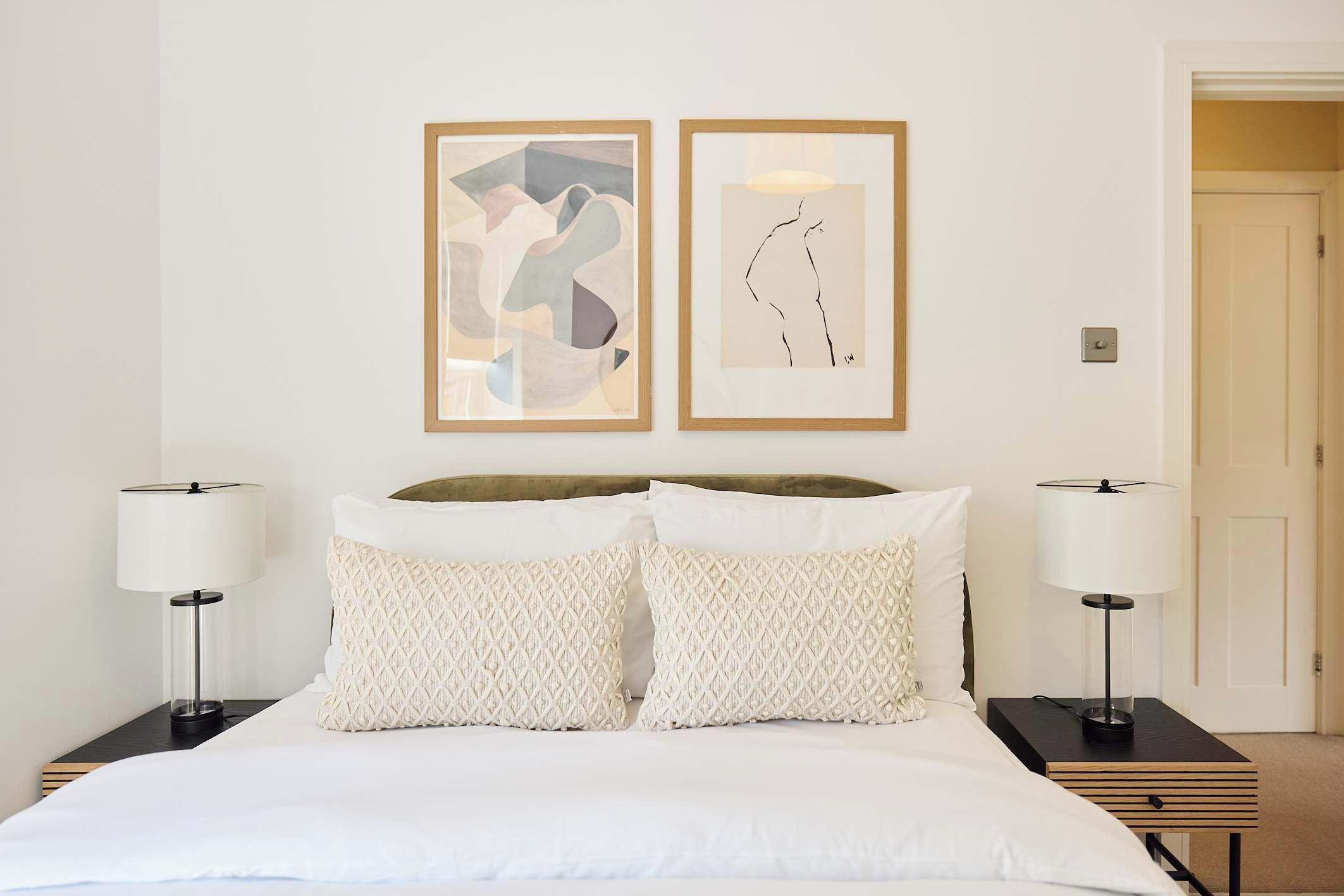 Habitación de hotel con cama, dos lámparas de noche y dos cuadros enmarcados en la pared.