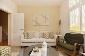 Ein Wohnzimmer mit einer Couch, einem grünen Sessel, einem Couchtisch und einem Gemälde an der Wand.