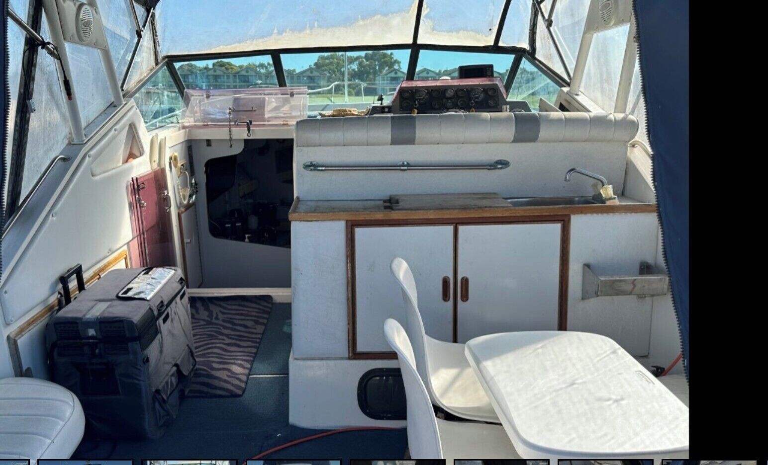 A boat interior with a small table, a white chair, a cabinet, and a control panel.