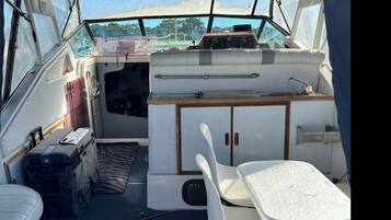 A boat interior with a small table, a white chair, a cabinet, and a control panel.