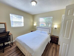 Un dormitorio con una cama, un escritorio y dos ventanas con persianas.