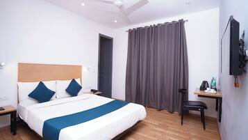 A hotel room with a bed, a desk with a chair, a ceiling fan, and a window with curtains.