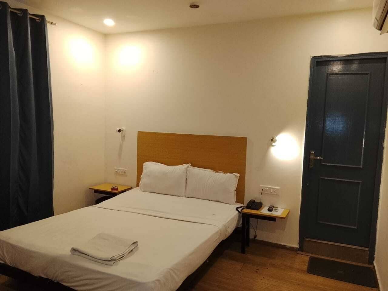 Una habitación de hotel con cama, mesitas de noche, teléfono y puerta.