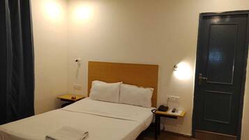 Una habitación de hotel con cama, mesitas de noche, teléfono y puerta.