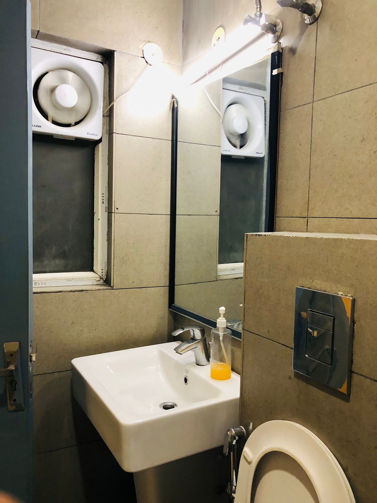 A bathroom with a white sink, a mirror, a toilet, and a soap dispenser.
