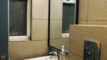 A bathroom with a white sink, a mirror, a toilet, and a soap dispenser.