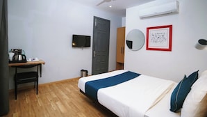 Quarto de hotel com cama, escrivaninha, cadeira, televisão, guarda-roupa, espelho e ar condicionado.