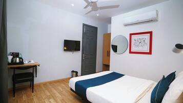 A hotel room with a bed, a desk, a chair, a television, a wardrobe, a mirror, and an air conditioning unit.