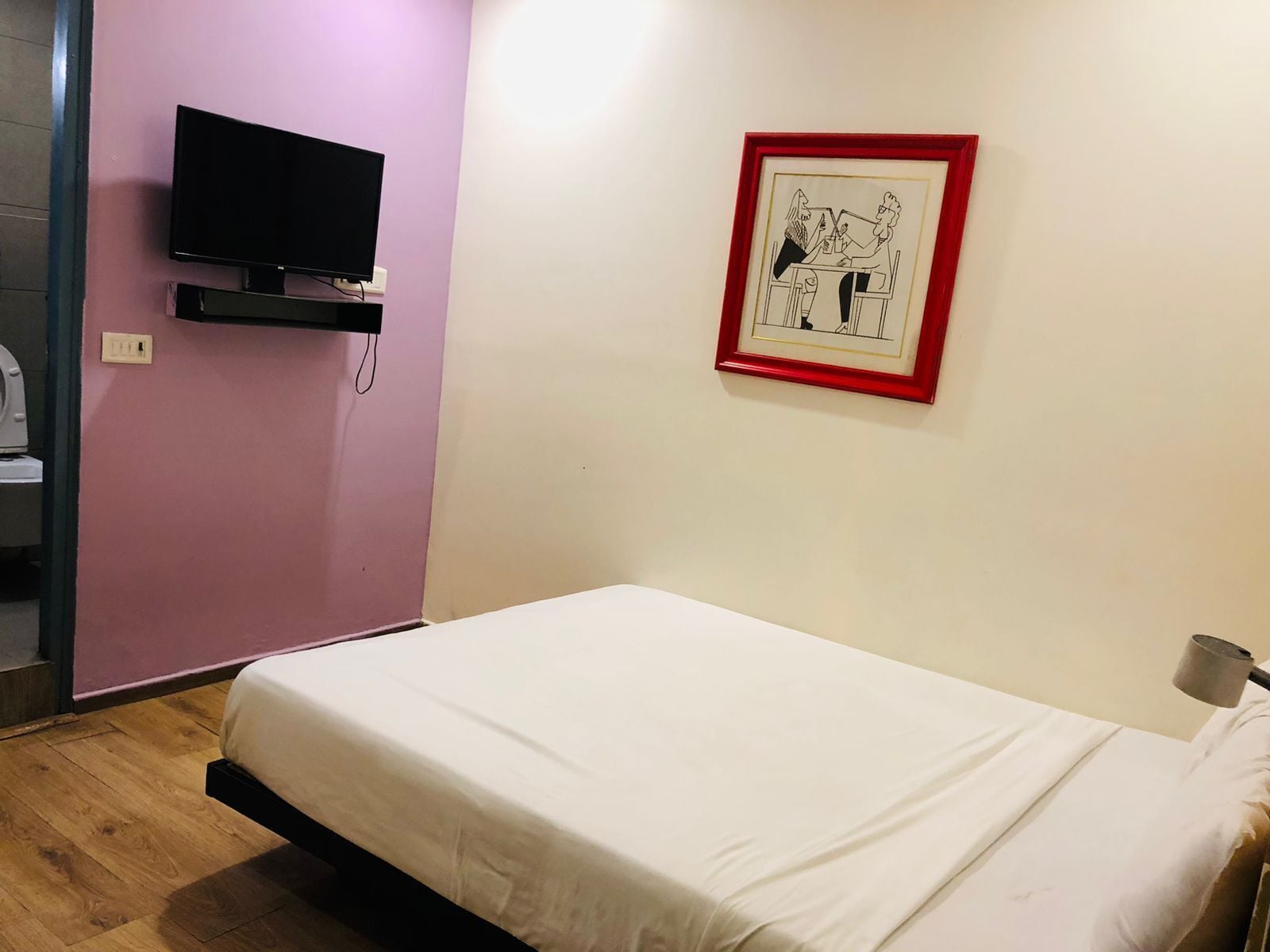 A room with a bed, a television on a stand, and a framed picture on the wall.