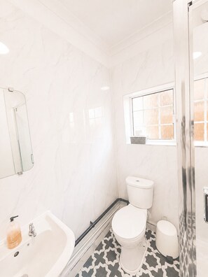 A bathroom with a white toilet, a sink, and a shower area. - Modern 2-Bedroom Flat near Crystal Palace (Greater London)