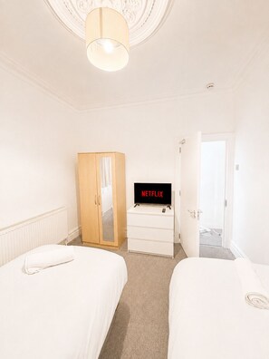 A hotel room with two beds, a wardrobe, a television, and a door leading to another room. - Modern 2-Bedroom Flat near Crystal Palace (Greater London)