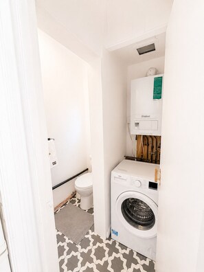 Une petite buanderie équipée d’un lave-linge, de toilettes et d’un chauffe-eau.